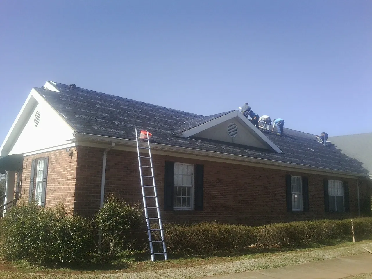 Crew tearing shingles off a brick ranch roof with a ladder set — Emergency Roof Repair work by our crew in New Harmony
