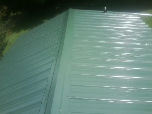 New green metal panels meeting at the ridge of a roof — Flat Roof Repair work by our crew in New Harmony