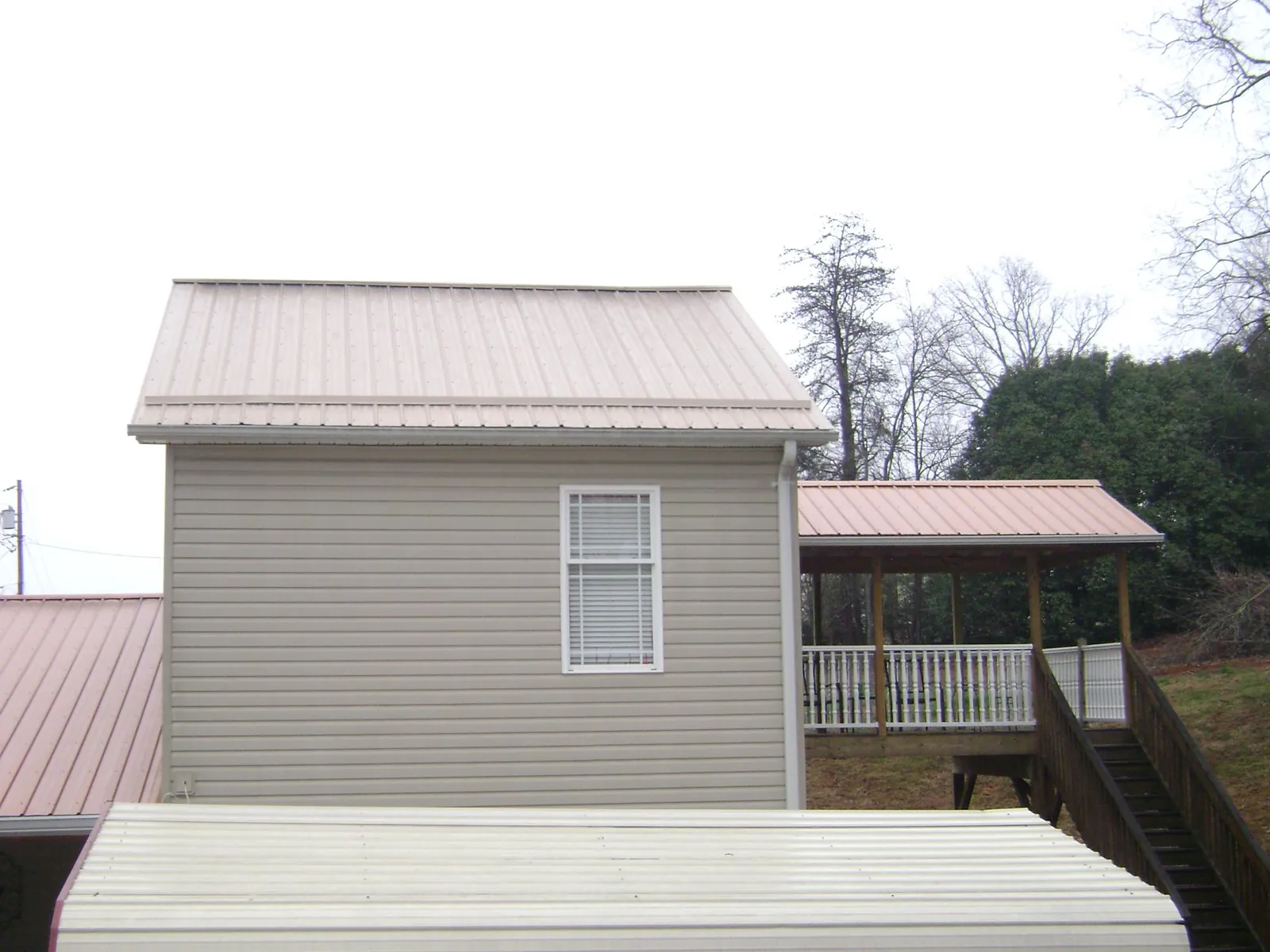 Tan metal roofs on a two story addition and attached porch, from a Roof Replacement job in New Harmony